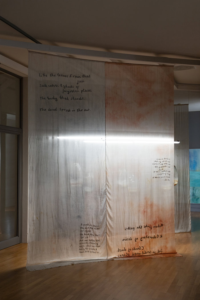 gefärbte Stoffbahnen mit handgeschriebenen Texten hängen von der Decke