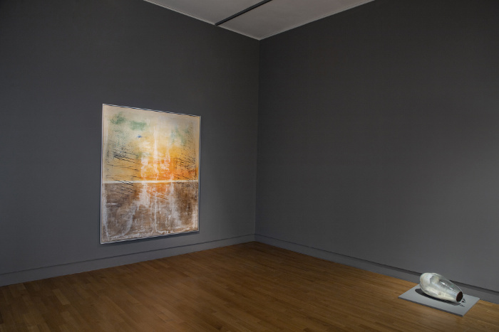 Blick in die Ausstellung mit Bild an der Wand und einem auf dem Boden liegenden Objekt