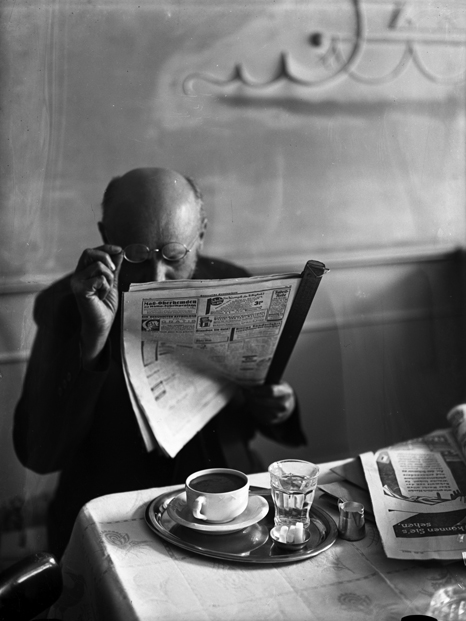 schwarz-weißes Foto eines zeitungslesenden Mannes im Café