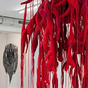eine rote, wurzelartige Skulptur hängt von der Decke eines Raums
