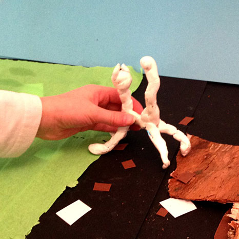 eine Hand hält eine Figur aus Knete in eine Papierkulisse